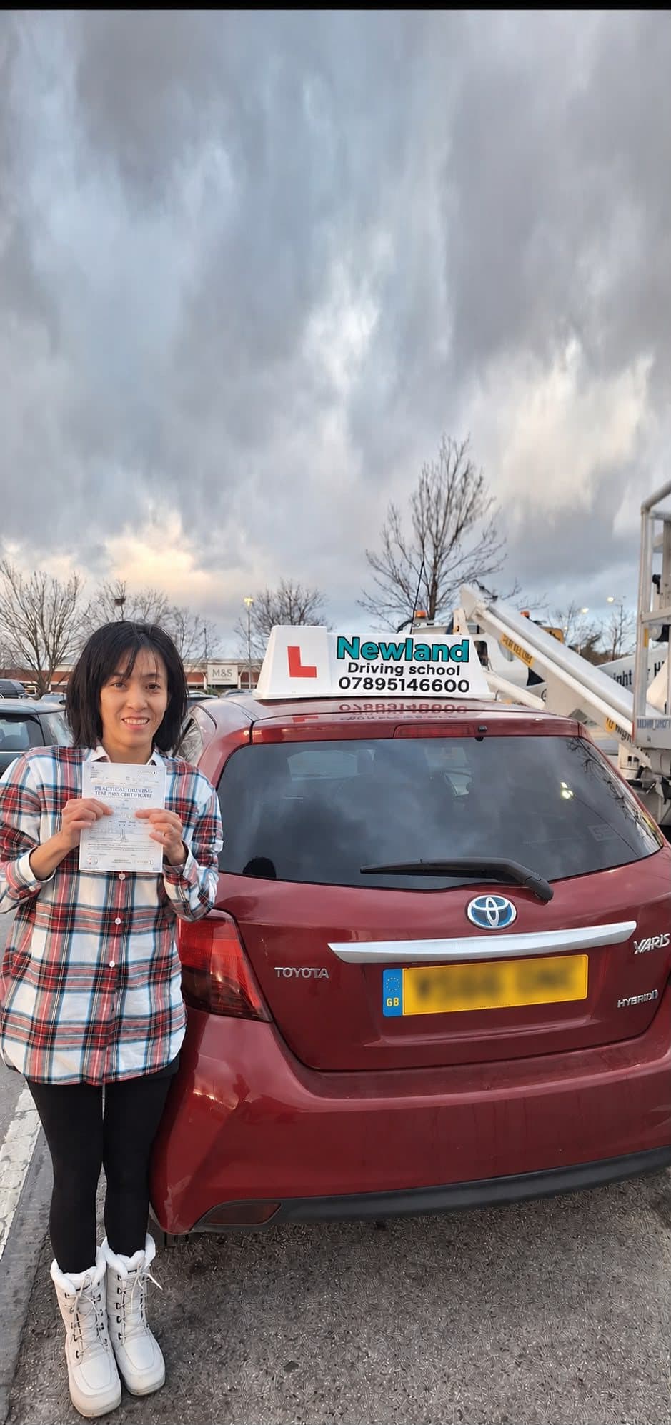 Smiling pupil holding a practical driving test pass certificate beside the Newland Driving School Toyota Yaris